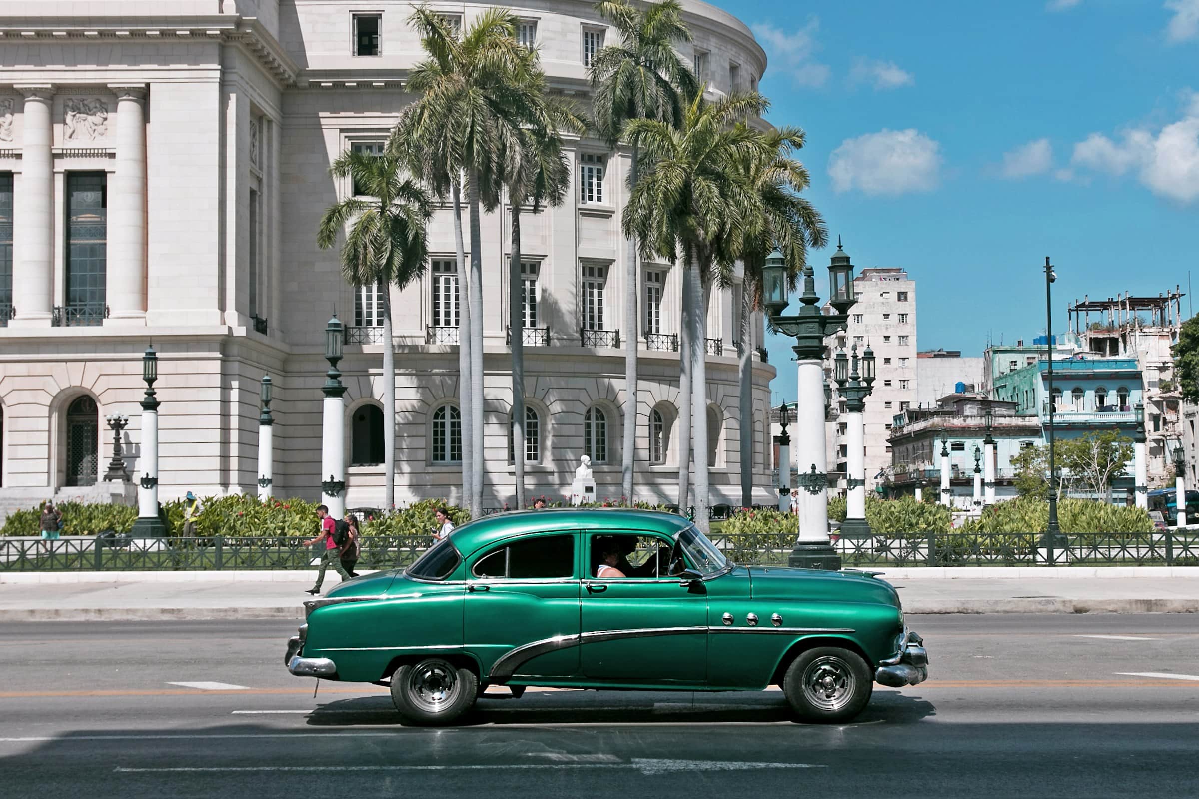 A vintage green car passing the domed Capitolio building in Havana, Cuba