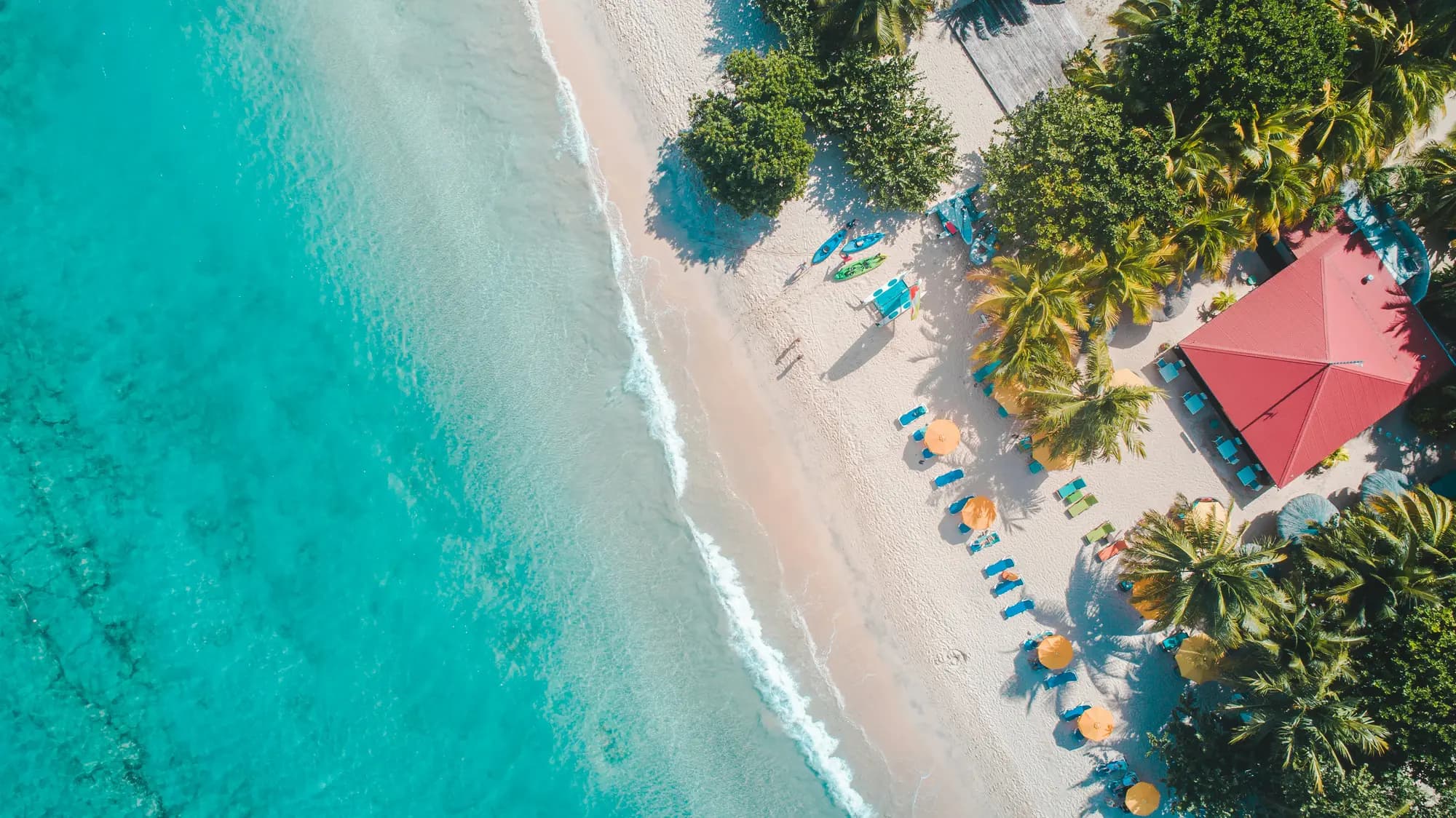 Aerial view of a tropical beach with kayaks, palms and a red-roofed resort