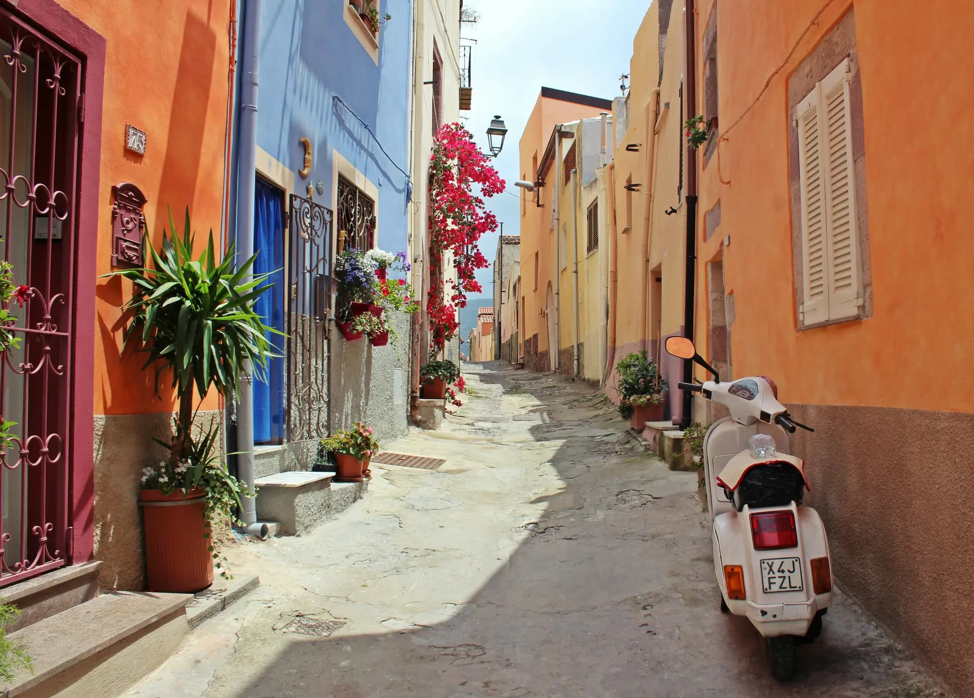 Narrow street of orange and ochre houses with pink bougainvillea and a white scooter