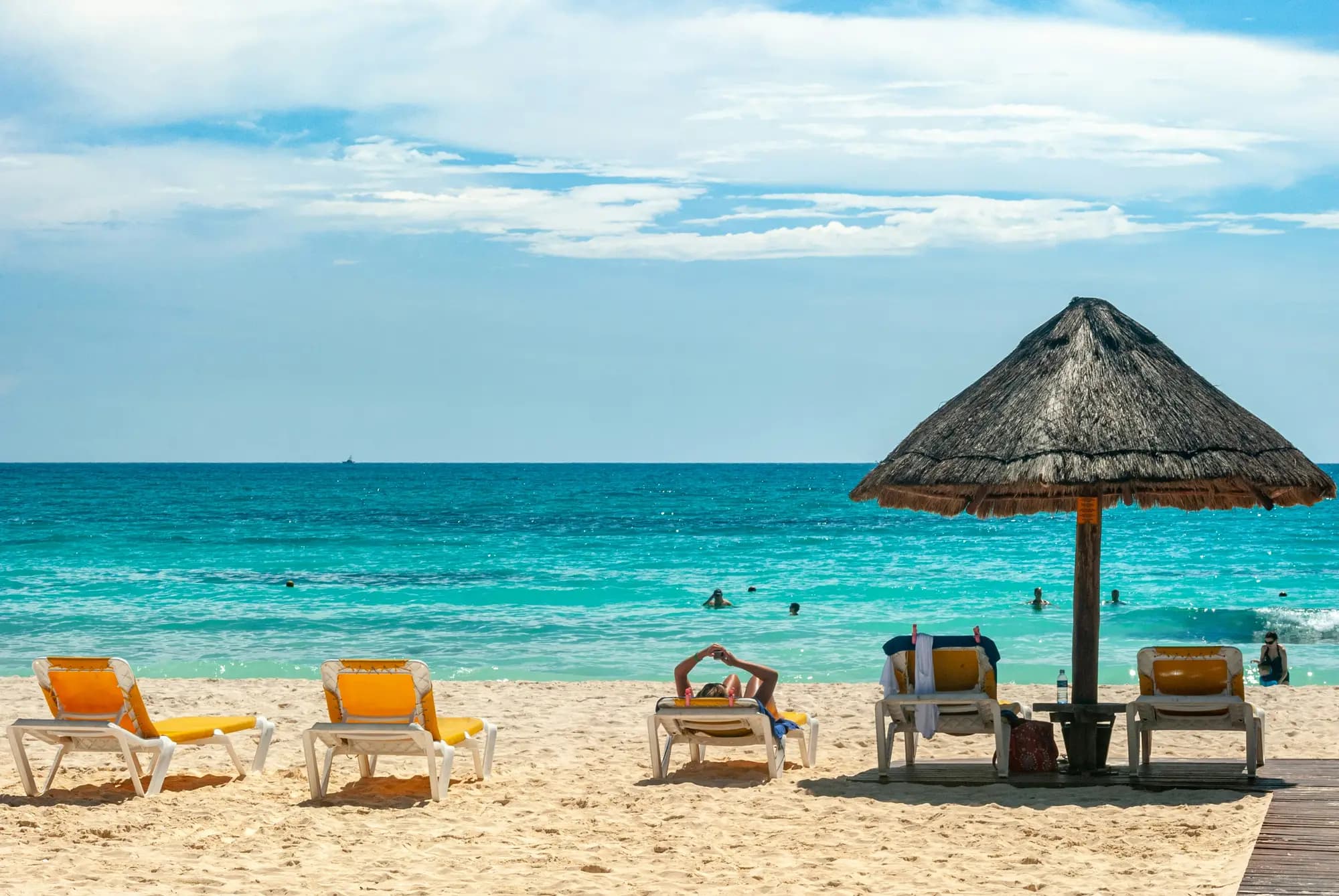 Yellow beach loungers and a thatched palapa on a white-sand beach facing a turquoise sea